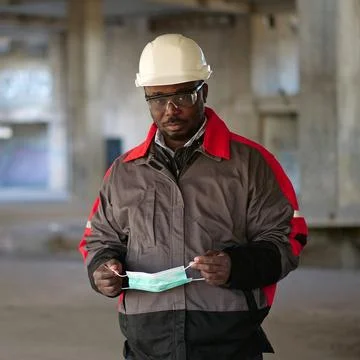 African american builder stands at construction site and holds medical mask Stock Photos