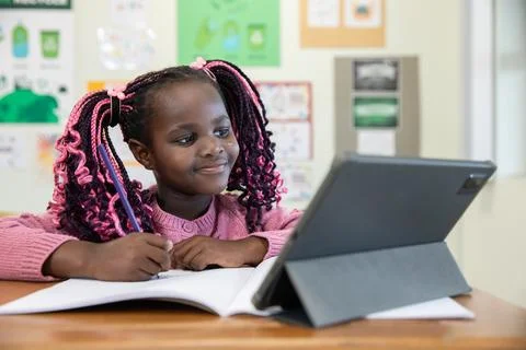 African american child scribbling notes with pencil in notebook and watching Stock Photos