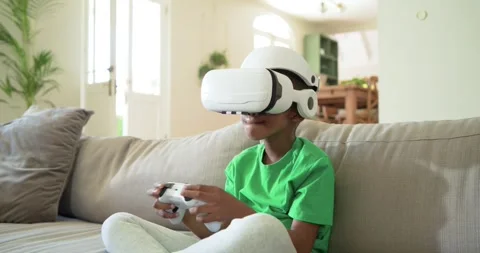 African-American child sitting on couch with VR headset and controller, reacting Stock Footage 340069853