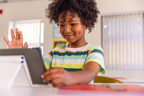African American child using tablet on stand at school desk, wearing striped Stock Photos