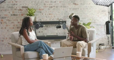 African American co-hosts sitting in studio by brick wall, man initiating Stock Footage 340070141