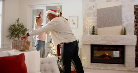 African American couple decorating tree for Christmas at home, man coming Stock Footage 343469346