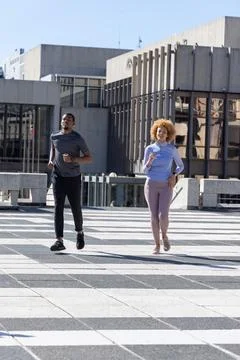 African American couple jogging on patterned pavers at plaza, wearing athletic Stock Photos