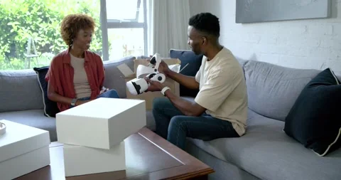 African American couple opening package on gray sofa man showing white VR Stock Footage 344851202