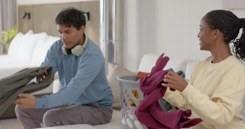 African American couple pulling laundry from basket on couch at home, folding to Stock Footage 346644649