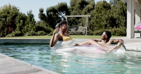 African American couple relaxing on float in sun woman in swimsuit holding glass Stock Footage 342929430