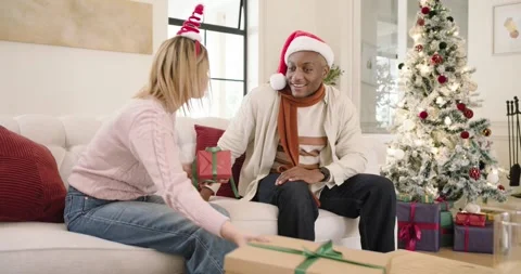 African American couple on sofa exchanging Xmas gifts woman giving red gift man Stock Footage 344679202