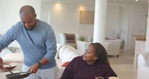 African American couple at table making breakfast man scooping eggs from pan Stock Footage 339495471