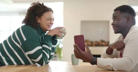 African American couple at table, man turning red phone to woman holding mint Stock Footage 342065680