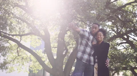 African American couple taking funny pictures together in front of a tree Stock Footage