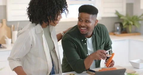 African American couple using peeler on carrot in kitchen, tablet guiding Stock Footage 344964761