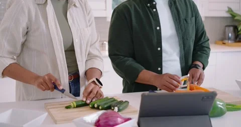 African American couple using tablet recipe at counter, woman slicing zucchini, Stock Footage 342843696