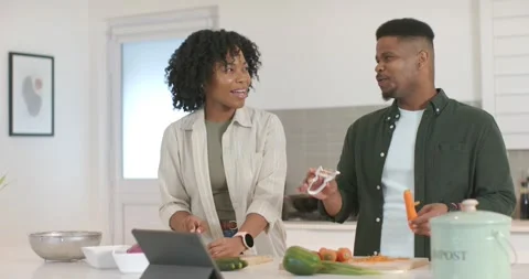African American couple using tablet recipe chopping veggies peeling carrot and Stock Footage 344964781
