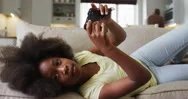 African American Daughter Lying On Couch Playing Video Game With Father In Stock Footage