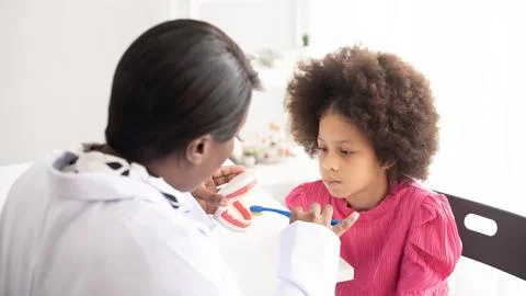 African American dentist explaining to child how to brush t.. Stock Photos
