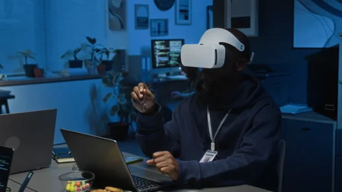 African American Developer Using VR Headset to Do Programming in Dark Office Stock Footage 329616535