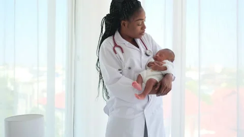 African American doctor hold newborn baby and look like she sing a song or talk Stock Footage 237799155