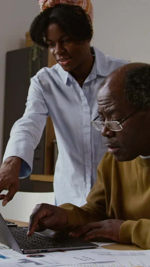 African American Elderly Man using Computer with Young Woman Helping Vertical Stock Footage 327686604