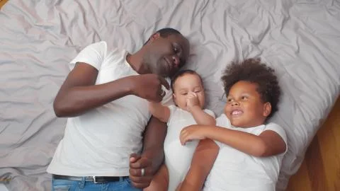African american father and children in casual clothe lying on bed at home Stock Photos