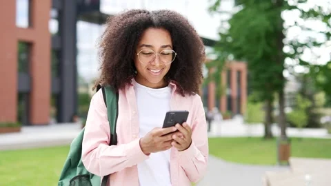 African american female student using phone standing on campus space near Stock Footage 302391984