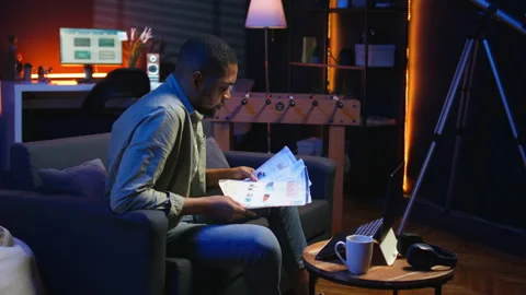 African american guy does research by reading articles and data driven papers Stock Footage 308260060