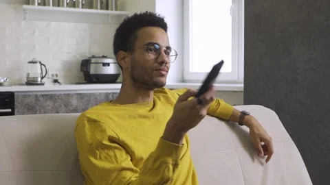 African-American guy with a remote control switches channels on TV Stock Footage 164056934