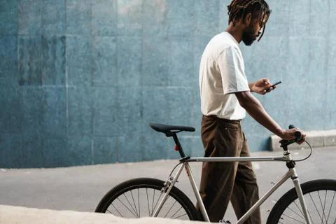 African american guy using cellphone while walking with bicycle Stock Photos