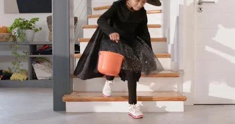 African American kid in witch hat descending home stairs placing pumpkin pail Stock Footage 345090082