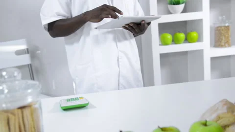 African American lab technician studying nutrition of food with a tablet compute Vídeo Stock 199629239