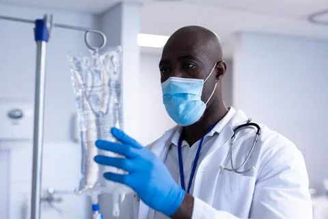 African american male doctor wearing face mask and gloves preparing iv drip bag Stock Photos