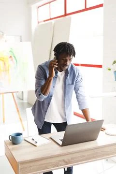 African american male painter at work using laptop and talking on smartphone in Stock Photos