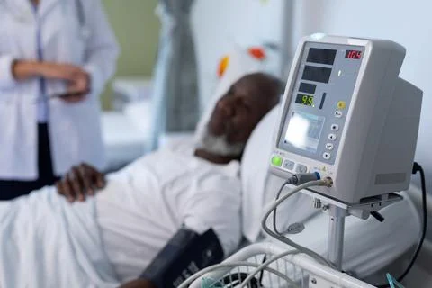 African american male patient lying on hospital bed next to blood pressure Stock Photos