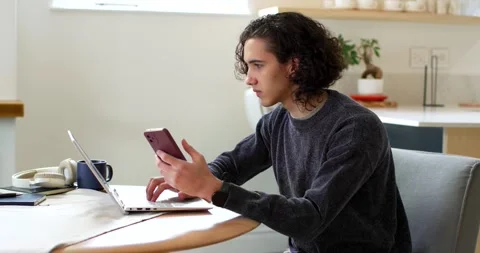 African American man 20s at kitchen table, glancing at pink phone, typing on Stock Footage 341027882