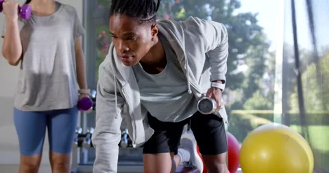 African American man adjusting bench rowing dumbbell as Asian woman curling Stock Footage 339497087