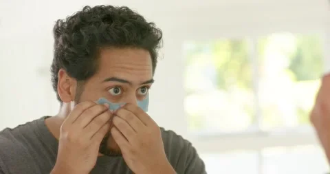 African American man applying 2nd blue undereye patch at mirror, smoothing to Stock Footage 336845084