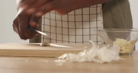 African American man in checked apron peeling and slicing garlic at home counter Stock Footage 340965187