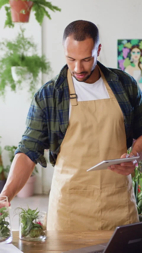 African American man checking green plants in flower shop and using tablet touch Vídeos de archivo 326003321