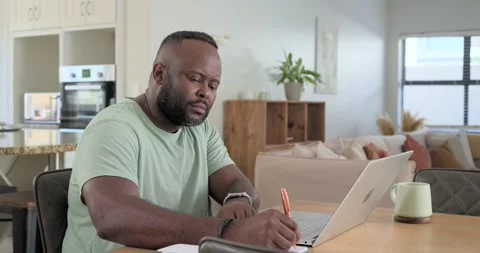 African American man checking smartwatch adjusting orange pen noting at home Stock Footage 342392977