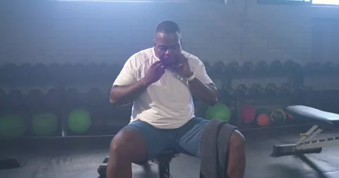 African American man checking watch, putting on headphones on bench at gym, Stock Footage 345071961