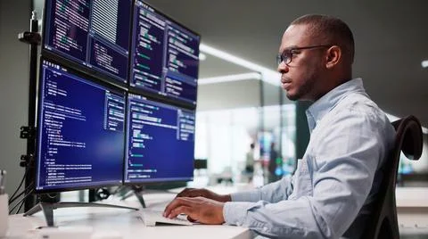 African American Man Coding On Multiple Computer Screens In Office. Foto stock