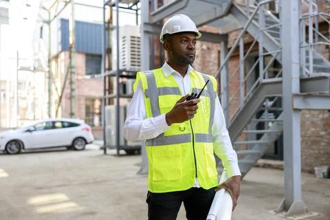 African american man controller in protective hardhat using walkie talkie for Stock Photos