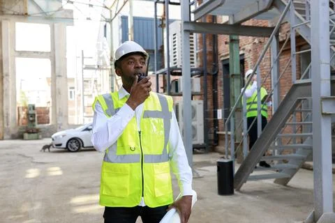 African american man controller in protective hardhat using walkie talkie for Stock Photos