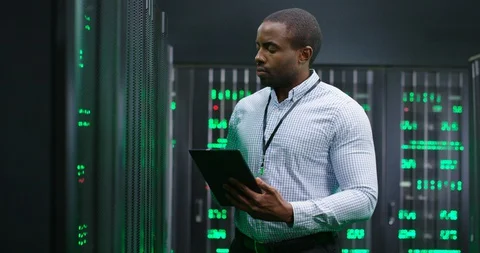 African American man, data base administrator in server room, tapping on tablet Video stock 128715196