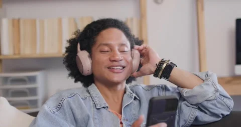 African American man in denim jacket touching headset tapping phone smiling on Stock Footage 337239201