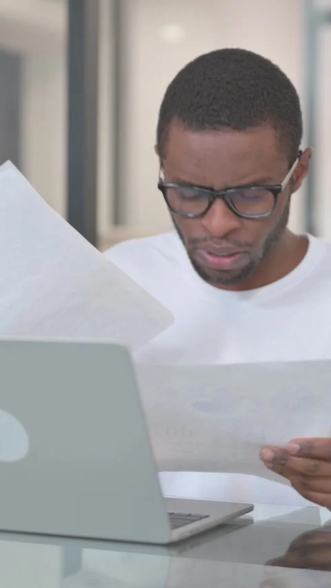 African American Man Doing Paperwork while Working on Laptop, vertical video Stock-Footage 324695437