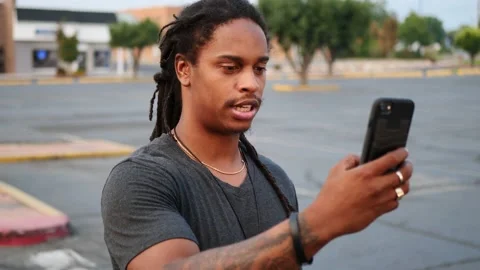 African American man with dreadlocks and tattoos pulls phone out to video Stock Footage 140679732
