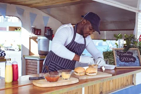African american man in food truck preparing order with hamburgers on worktop Stock Photos
