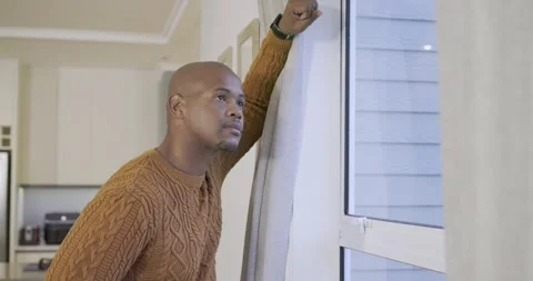 African American man glancing at kitchen window, pulling curtain and peering Stock Footage 336658156