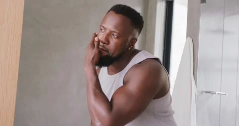 African American man leaning toward mirror checking and applying product to Stock Footage 342393045