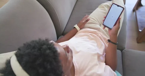 African American man lying on couch in pink tee tapping loading phone screen Stock Footage 338326269